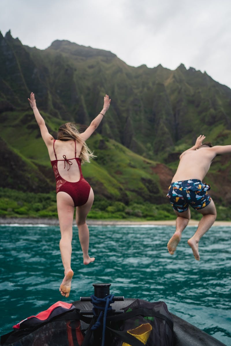 man and woman jumping towards body of water