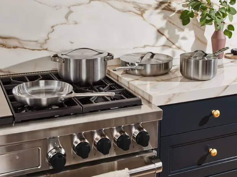 Stainless steel pots and pans from Caraway displayed on a kitchen countertop.