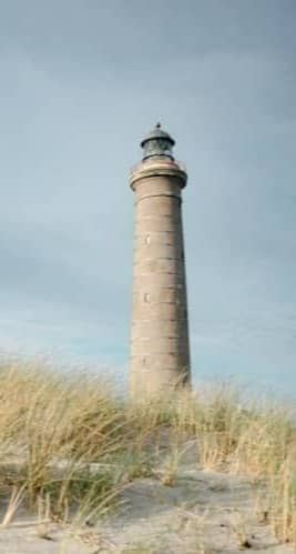Tall lighthouse on sandy dunes with dry grass.