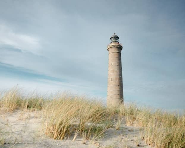 Tall lighthouse on sandy dunes with dry grass.