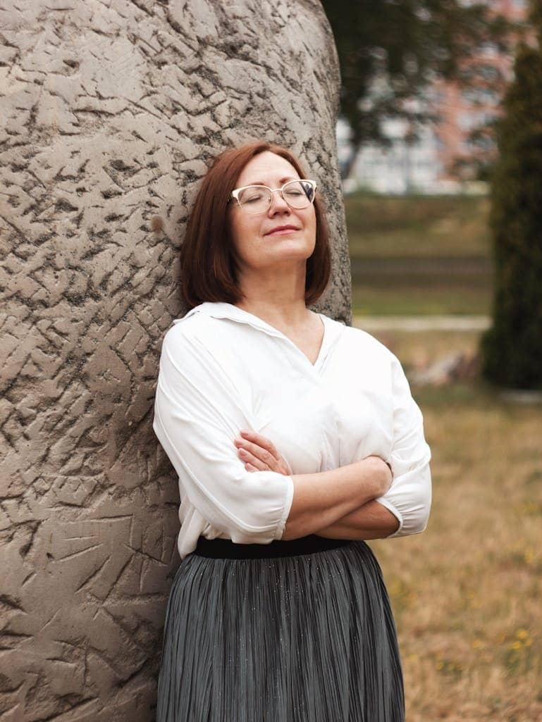 woman in white long sleeve shirt and black skirt standing beside brown tree during daytime