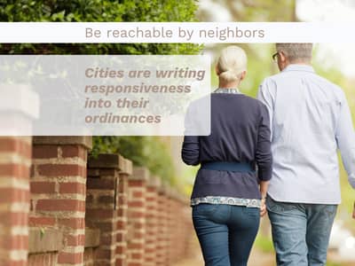 Rear view of a couple walking along a residential sidewalk next to a brick wall. Text overlay reads: "Be reachable by neighbors. Cities are writing responsiveness into their ordinances."