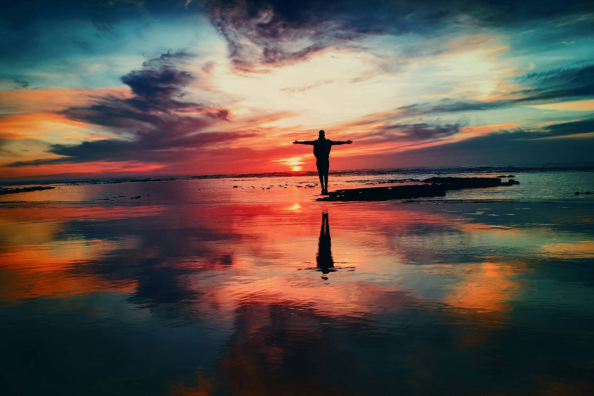 beautiful orange sunset sky and water with person with arms outstretched