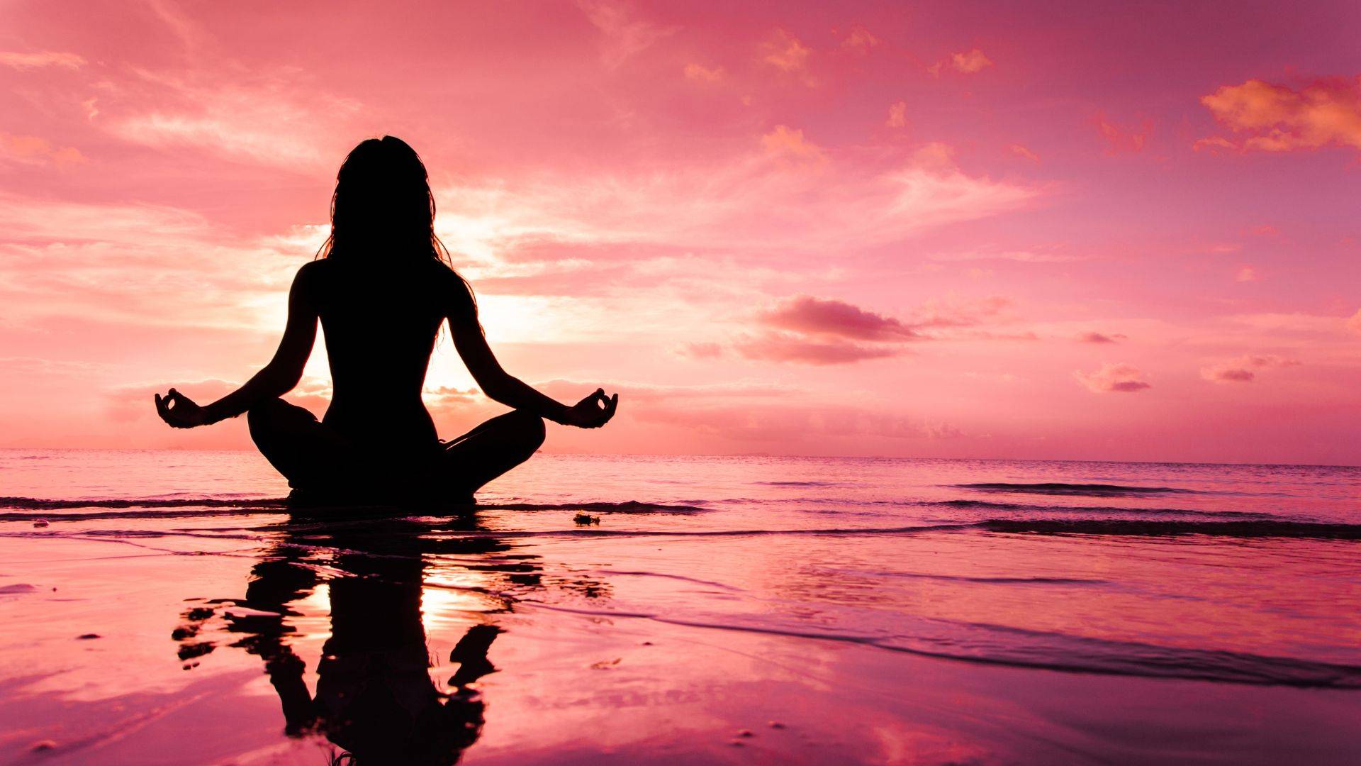 Silhouette of woman meditating in lotus position on a beach at sunset