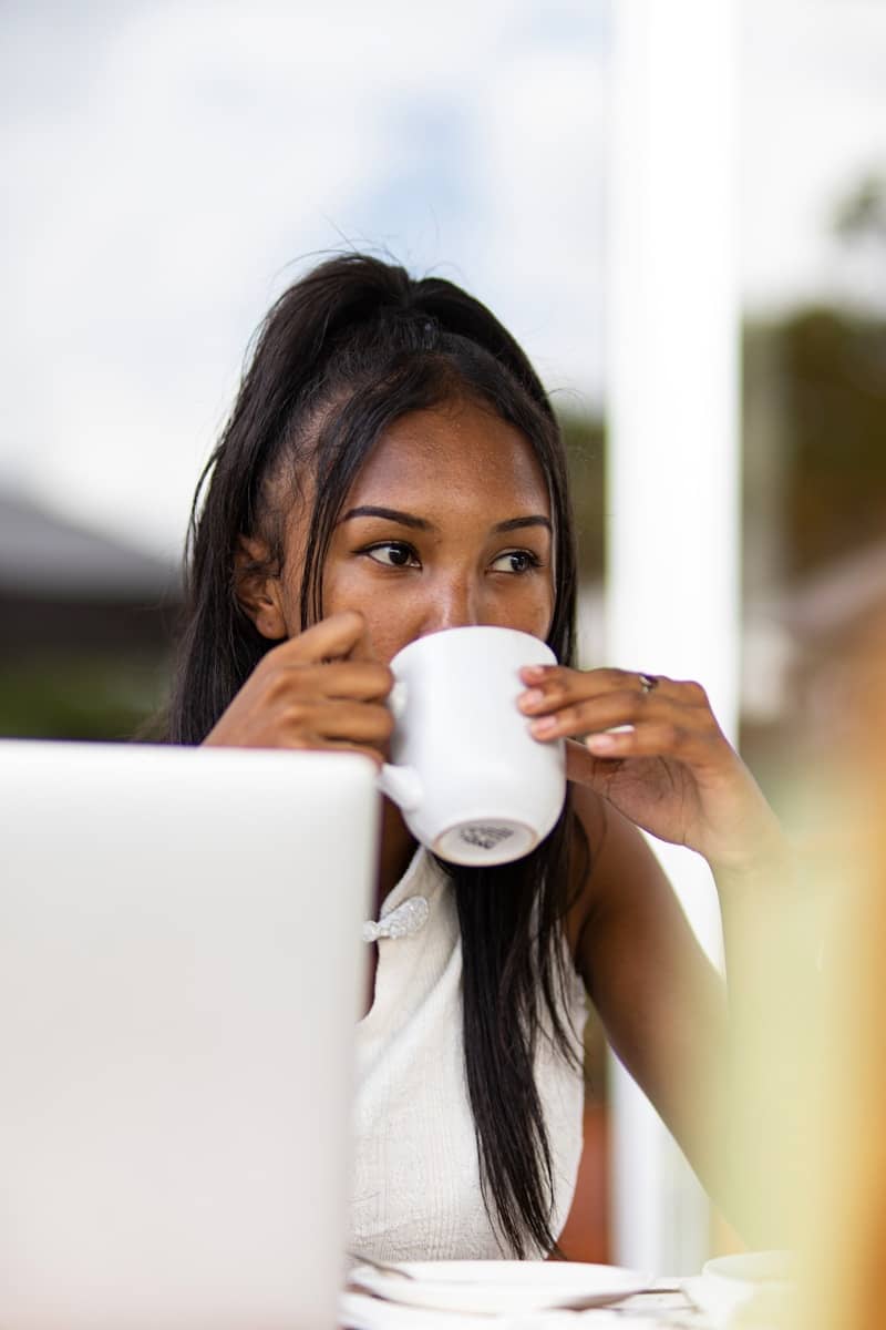Woman sips from a mug while working on a laptop.