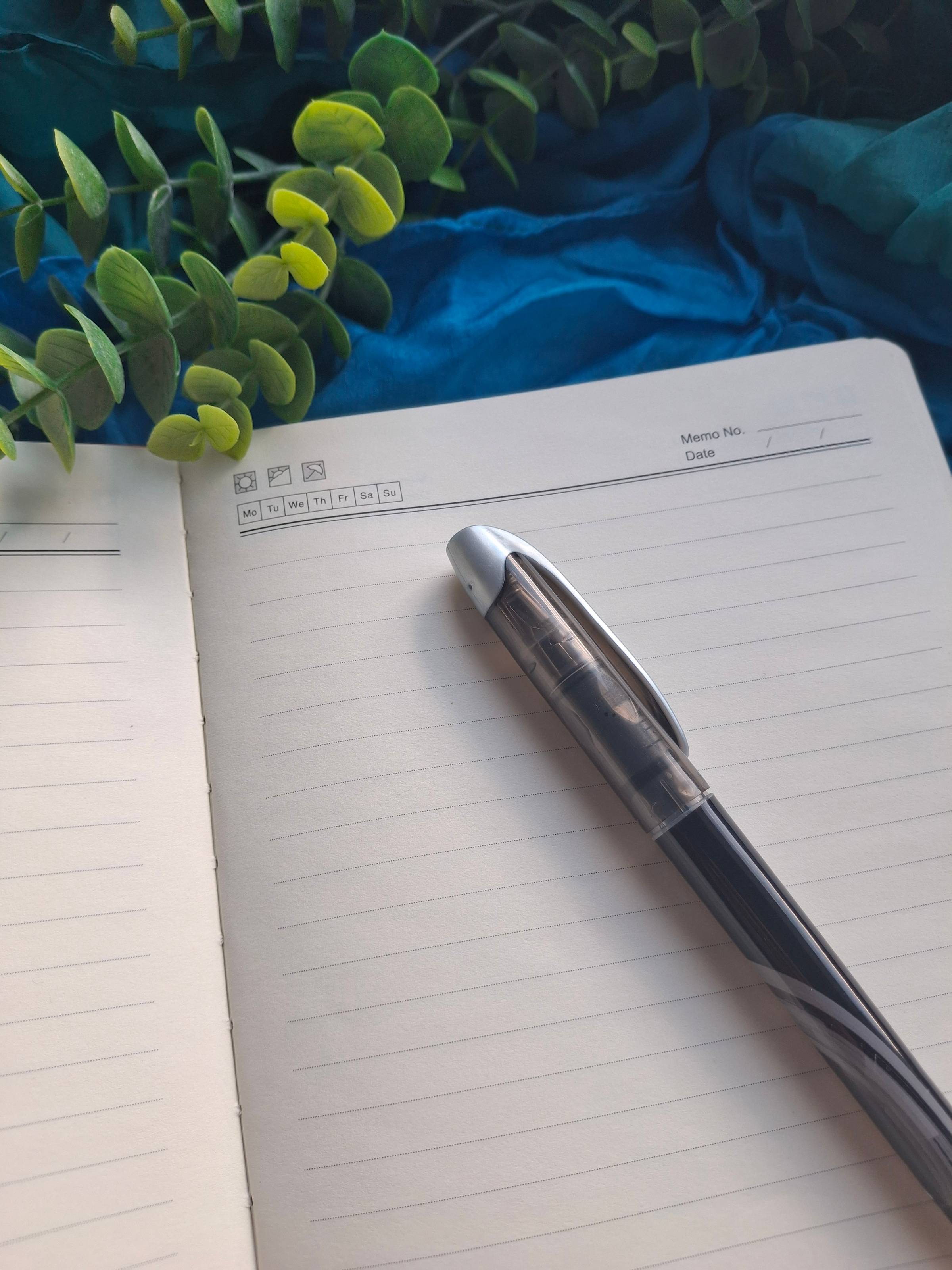 Peaceful image of journal page and fountain pen, with greenery and blue silk. 
