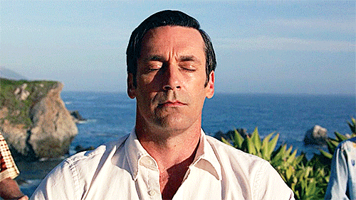 Don Draper from Mad Men sits on a cliff meditating with his eyes closed.
