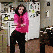 Woman in pink sweater dancing excitedly in a kitchen