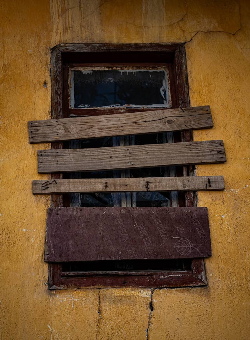 A boarded-up window on a yellow wall
