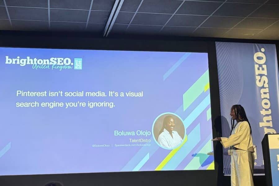 Photo of Boluwa Olojo presenting at brightonSEO. A large presentation slide behind her reads, “Pinterest isn't social media. It's a visual search engine you're ignoring.” The slide includes the brightonSEO branding and Boluwa's name and company, TalentDistro.