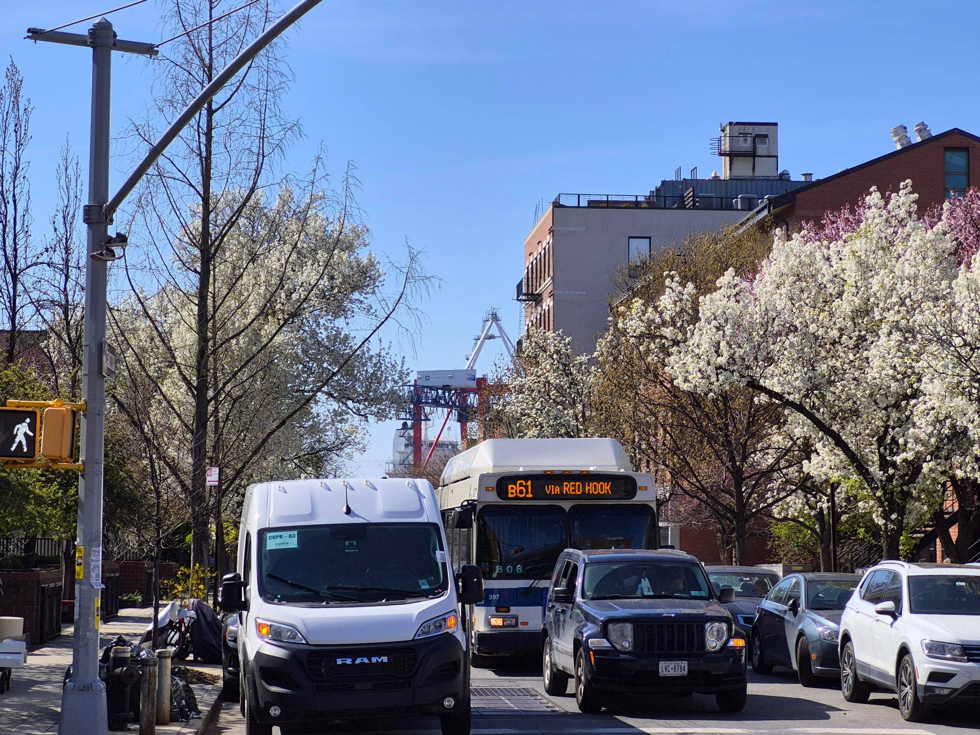 A picture of a street with bus, cars, flowering trees, and a port crane in the background