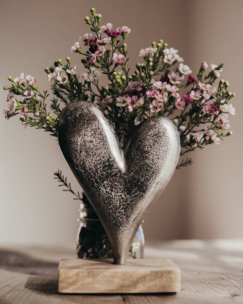 A heart shaped vase filled with flowers on top of a wooden table