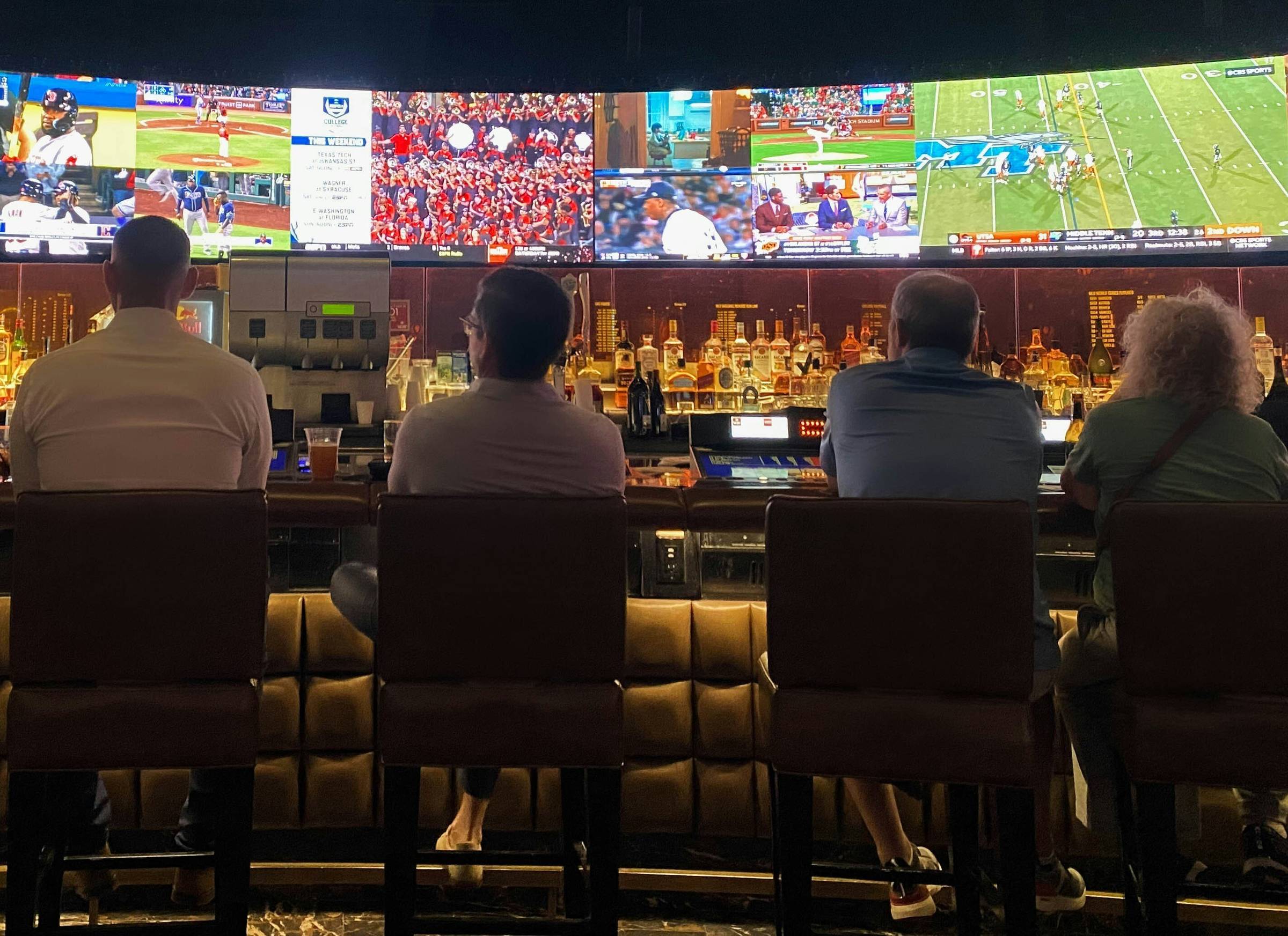 a group of people sitting at a bar watching sports on tv | The rapid growth of digital gambling in Europe was propagated by the emergence of digital technologies allowing anyone to place bets online | Mania Sports