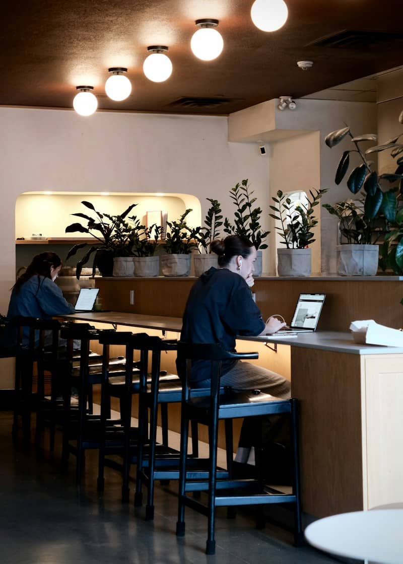 Two people working on laptops at a long counter in a cafe