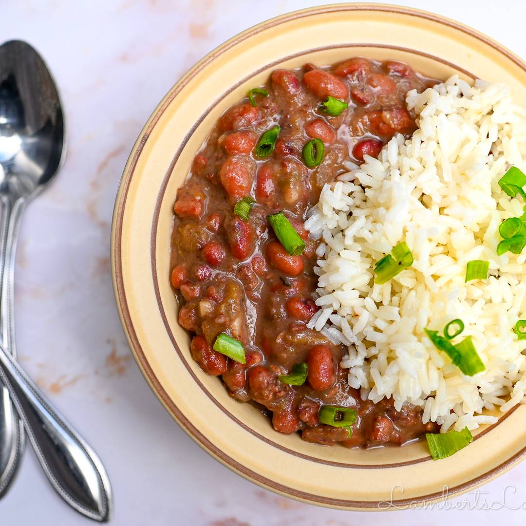 A tan bowl filled with a hearty serving of red beans and rice, garnished with fresh sliced green onions.