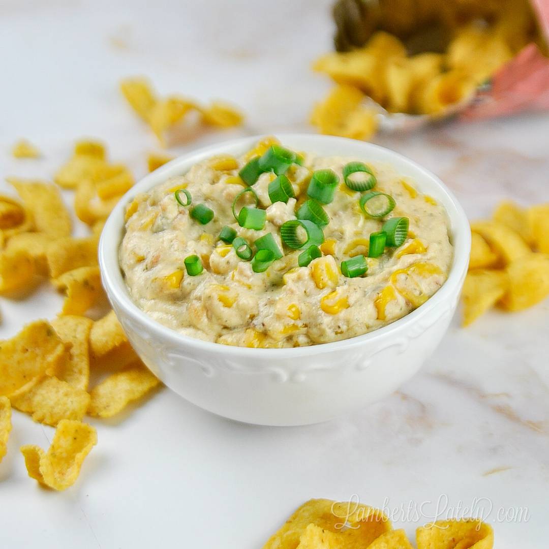 corn dip covered in green onions in a bowl, surrounded by corn chips.