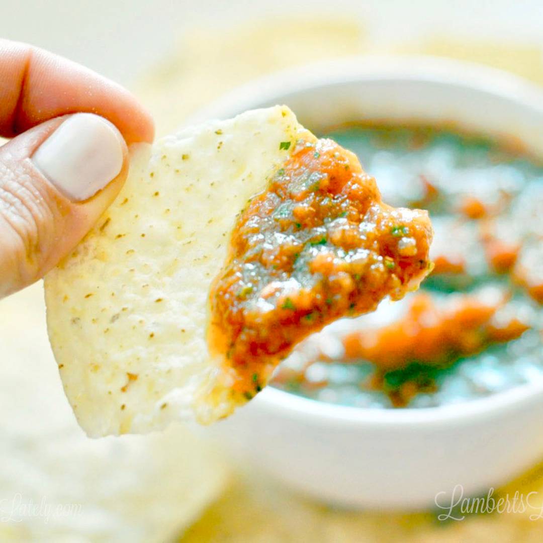 A close-up of a hand holding a tortilla chip scooping a large dollop of chunky, restaurant-style blender salsa.