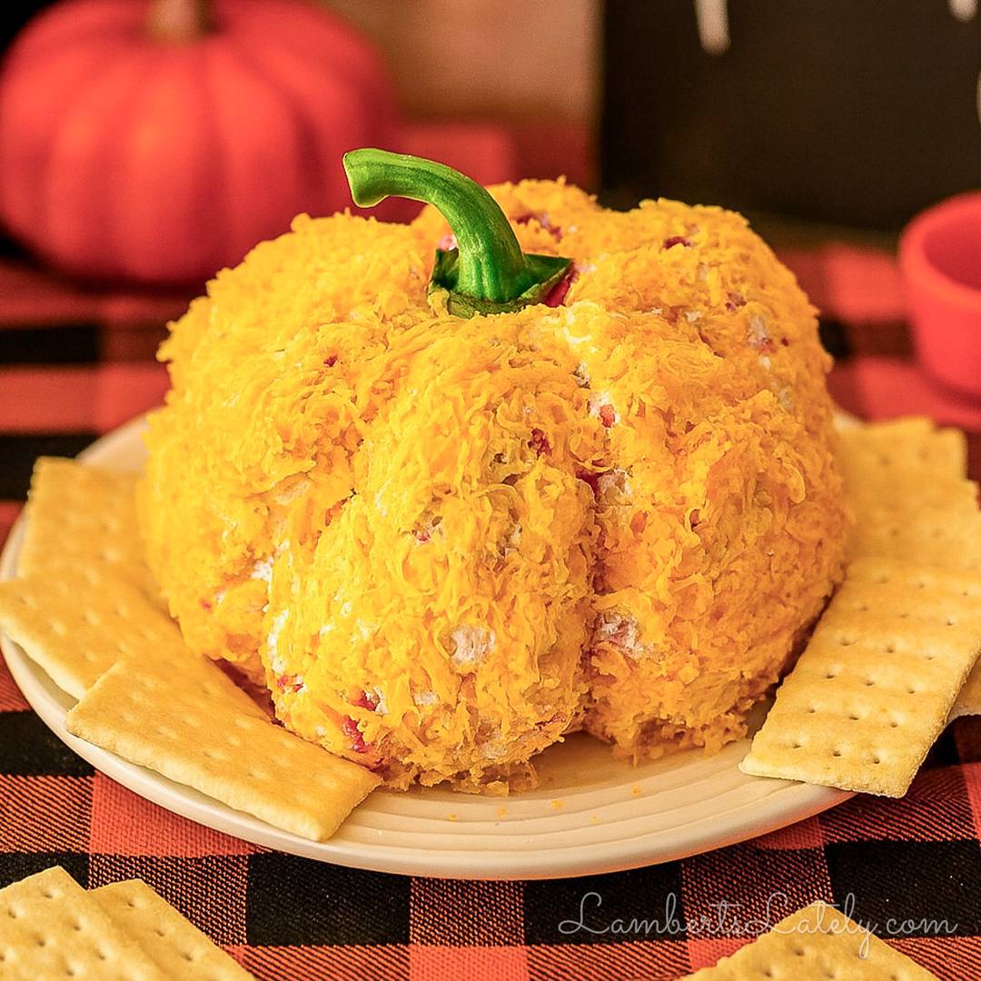 Pumpkin-shaped cheese ball coated in shredded cheddar and served with crackers.
