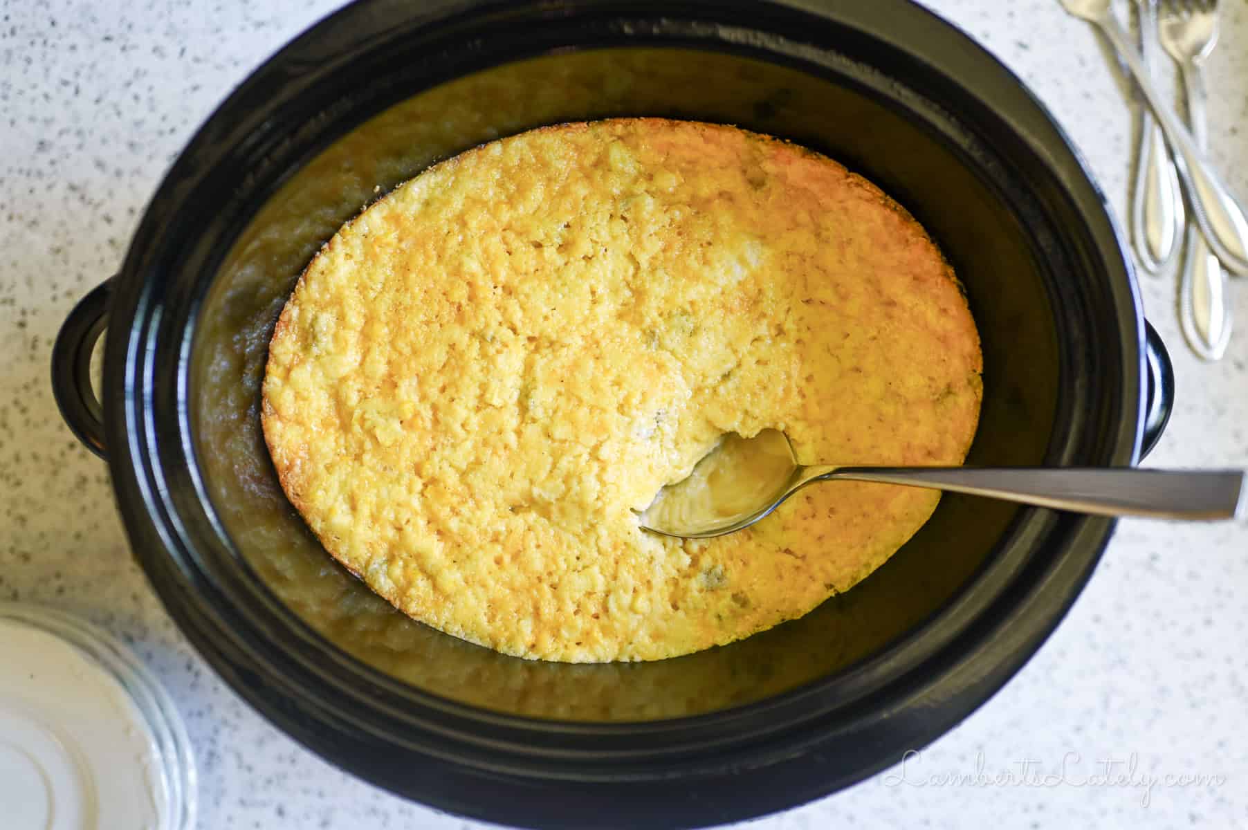 corn casserole and a spoon in a crock pot.