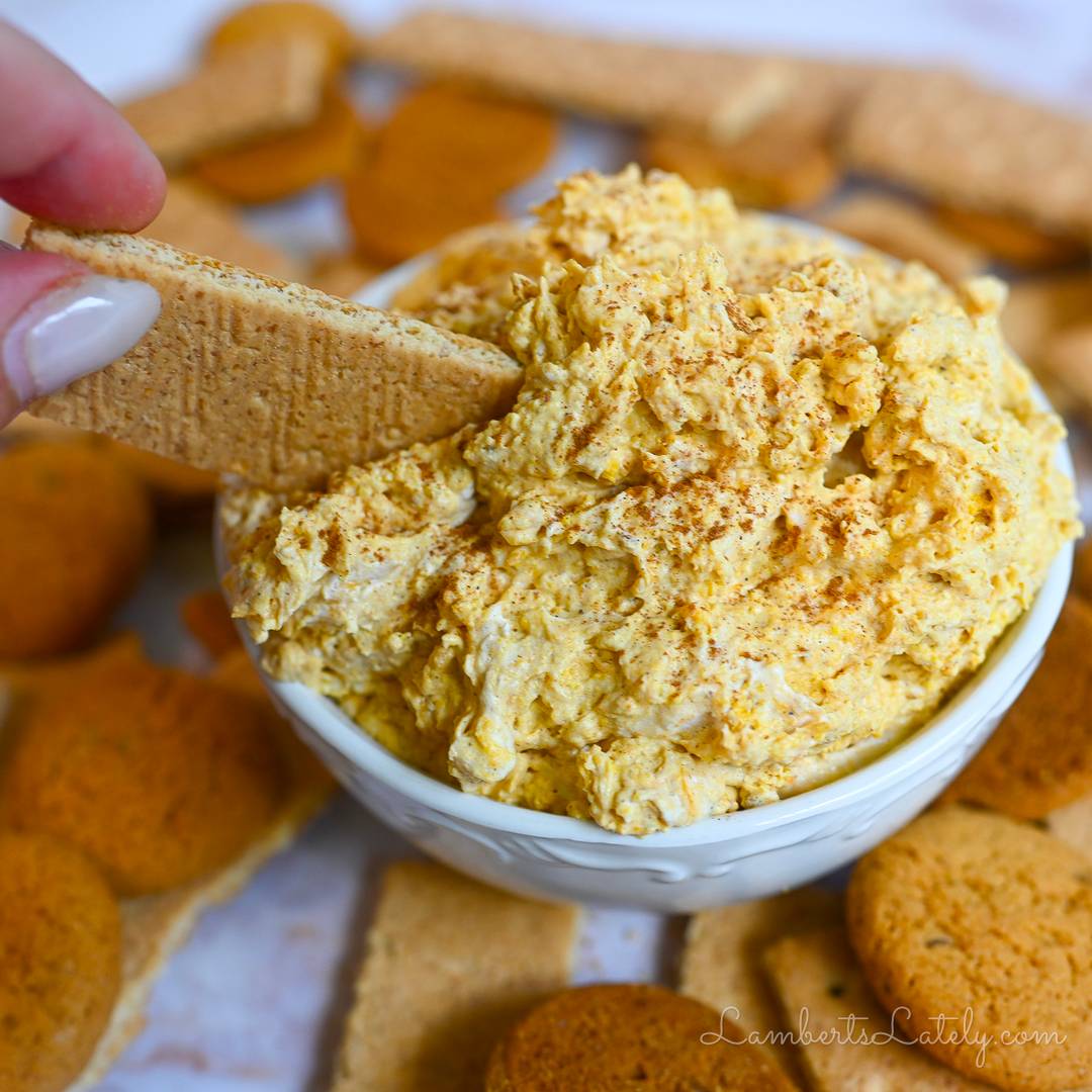 Creamy pumpkin fluff dip in a white bowl served with graham crackers and gingersnaps.