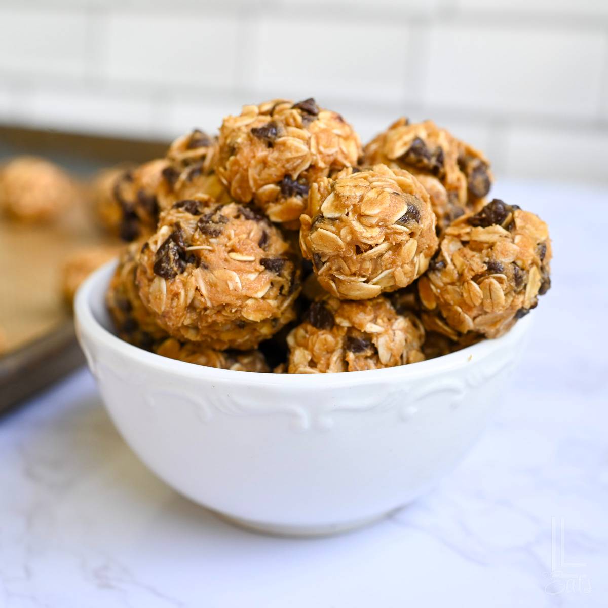 peanut butter oatmeal balls stacked in a white bowl in front of a cookie sheet.