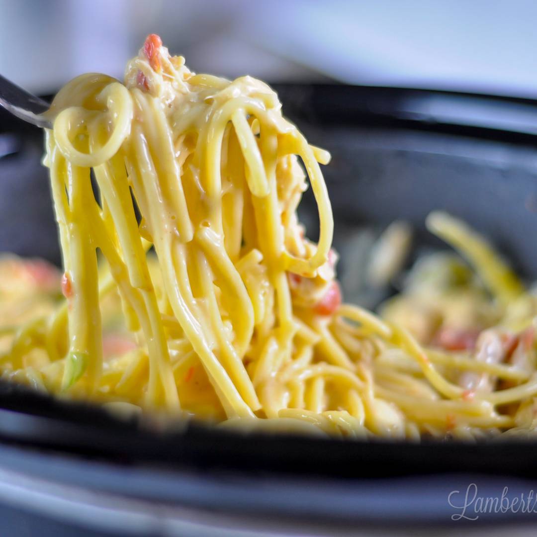 holding a large forkful of chicken spaghetti above a crock pot.