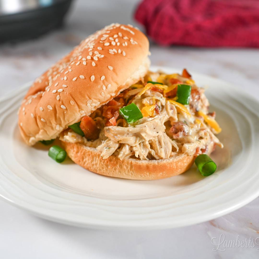 crack chicken in a sandwich bun, topped with green onions, bacon, and cheese.