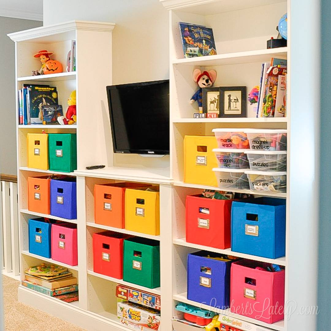 Built-in playroom shelving with colorful storage bins, labeled toy containers, books, puzzles, and games organized for easy access.