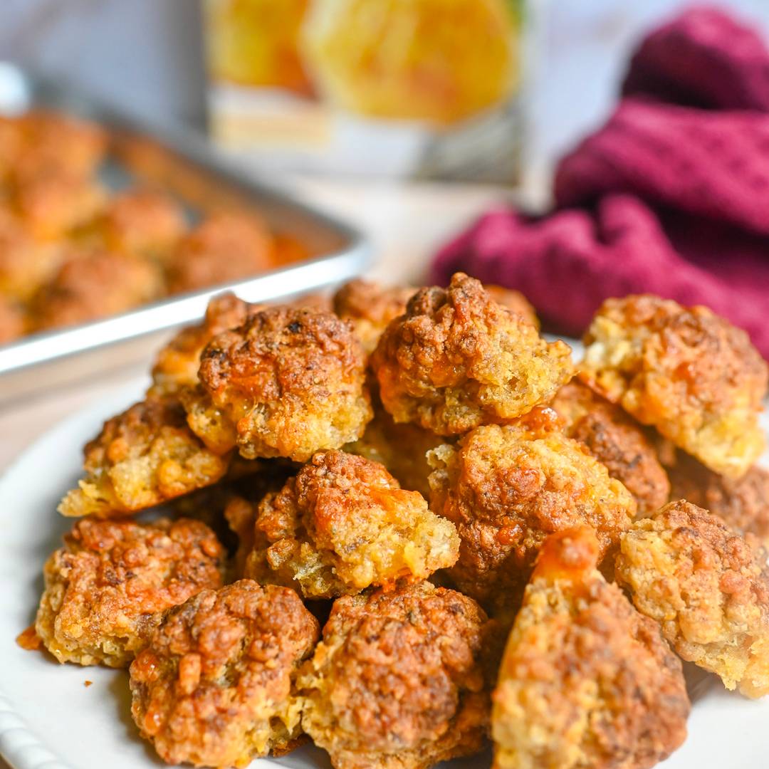 sausage balls stacked on a plate, in front of red lobster baking mix, sheet pan.