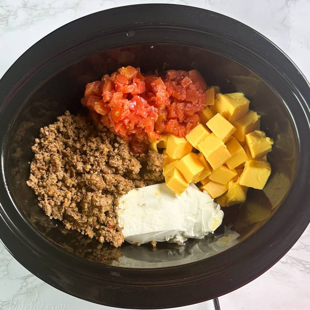 Ground sausage, diced tomatoes, Velveeta cheese, and cream cheese in a slow cooker before cooking.
