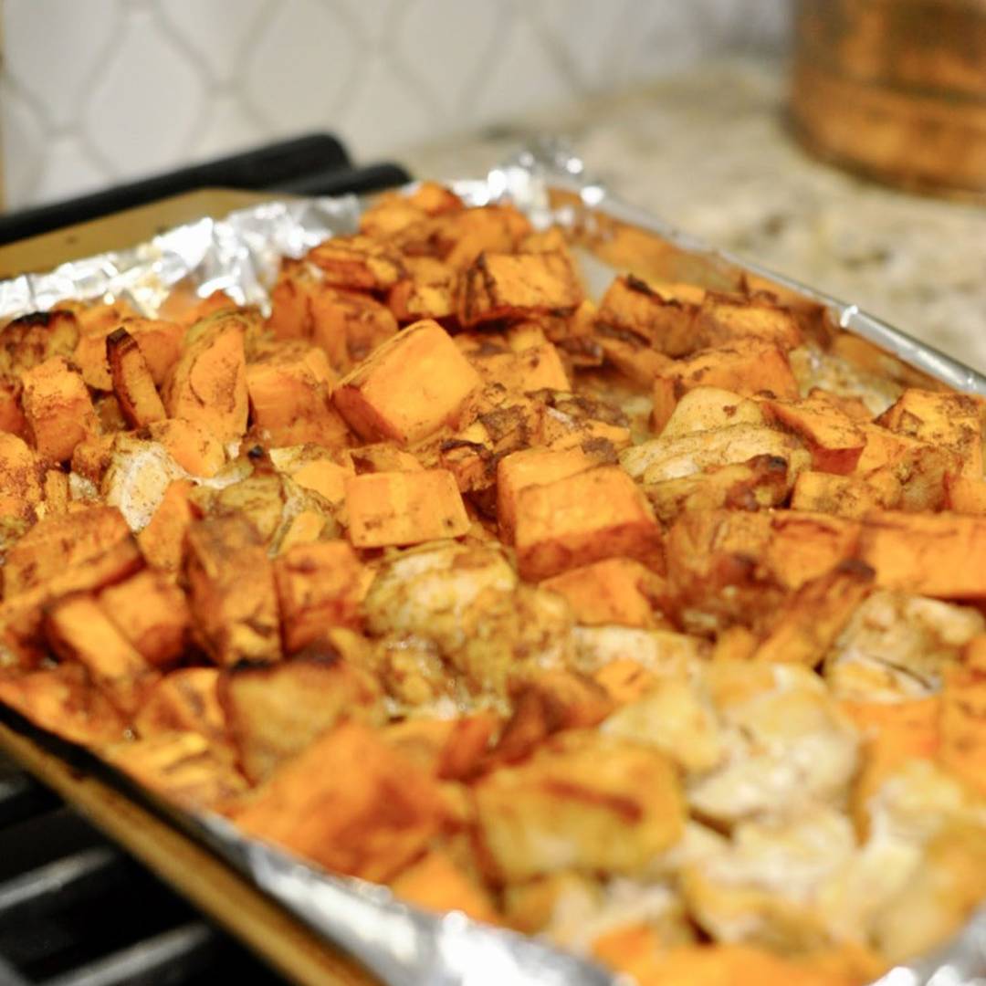 Cubed sweet potatoes and chicken pieces roasted to a golden brown on a foil-lined sheet pan, appearing seasoned and slightly caramelized.