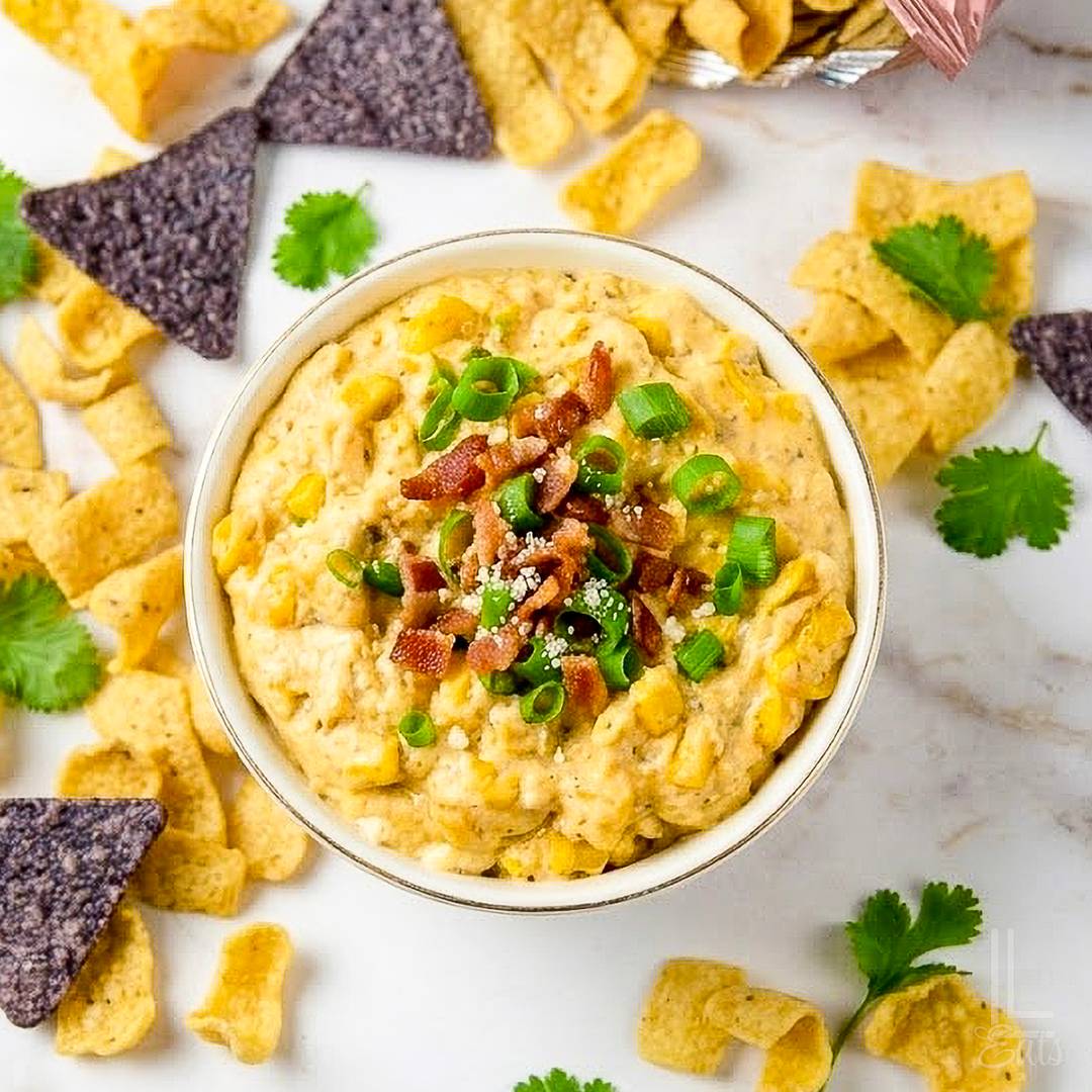 Creamy corn dip topped with bacon, green onions, and Parmesan cheese, served with corn and tortilla chips.