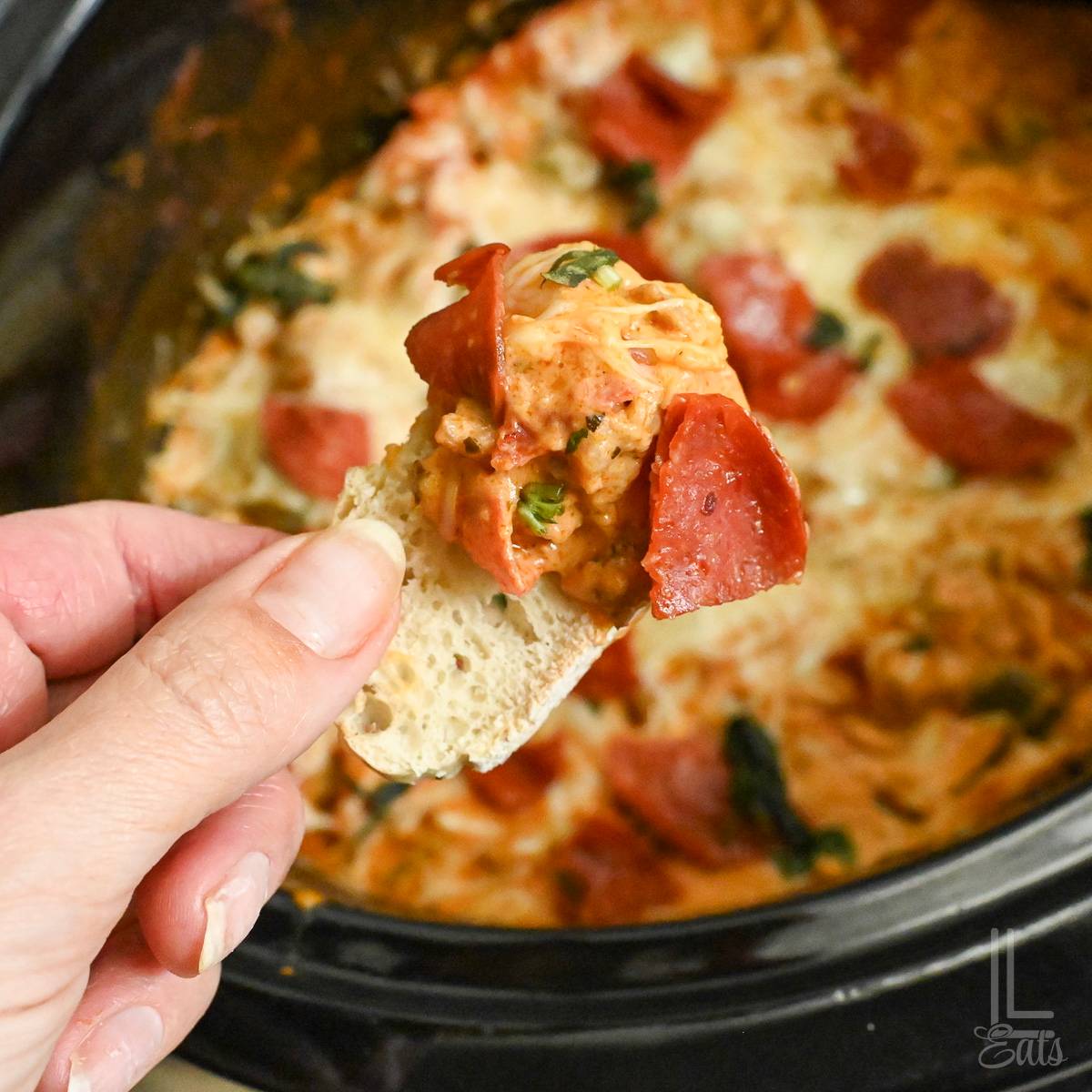 holding a bite of pizza dip on a piece of bread.