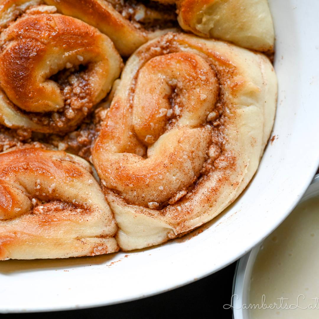 Freshly baked cinnamon rolls in a white baking dish, swirled with cinnamon sugar and lightly glazed.