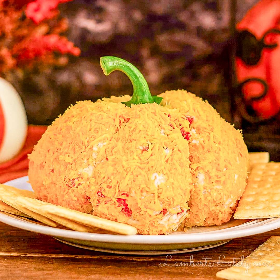 Pumpkin-shaped cheese ball coated in orange shredded cheese and served with crackers.