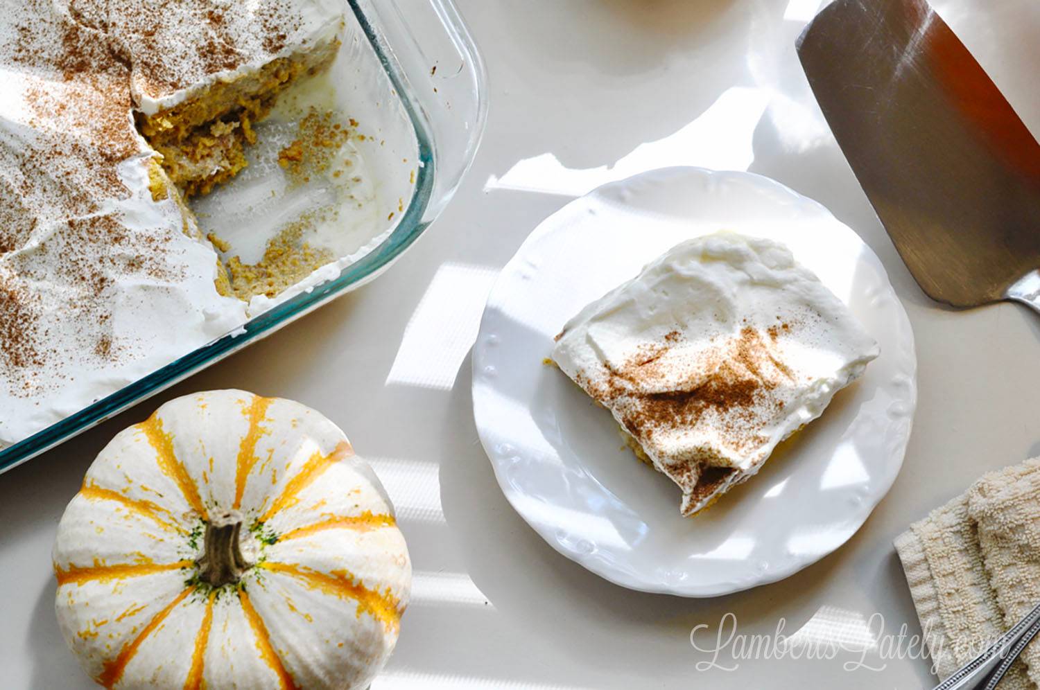 pumpkin tres leches cake in a baking dish, next to a serving on a plate, a pumpkin, and a serving knife.