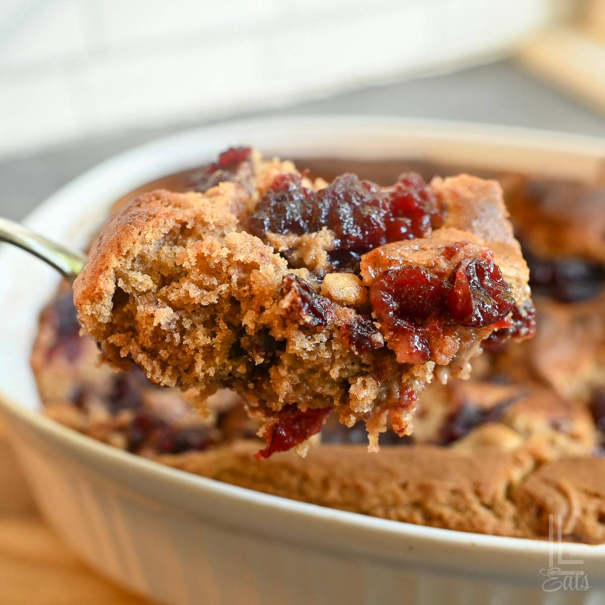 holding a spoonful of cranberry cobbler in front of a baking dish.