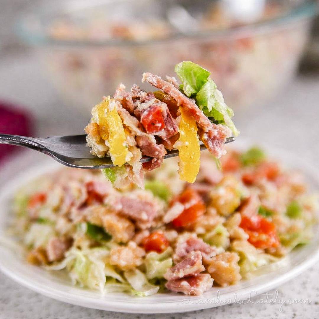 Forkful of Italian-style chopped salad with lettuce, deli meat, peppers, tomatoes, and cheese.