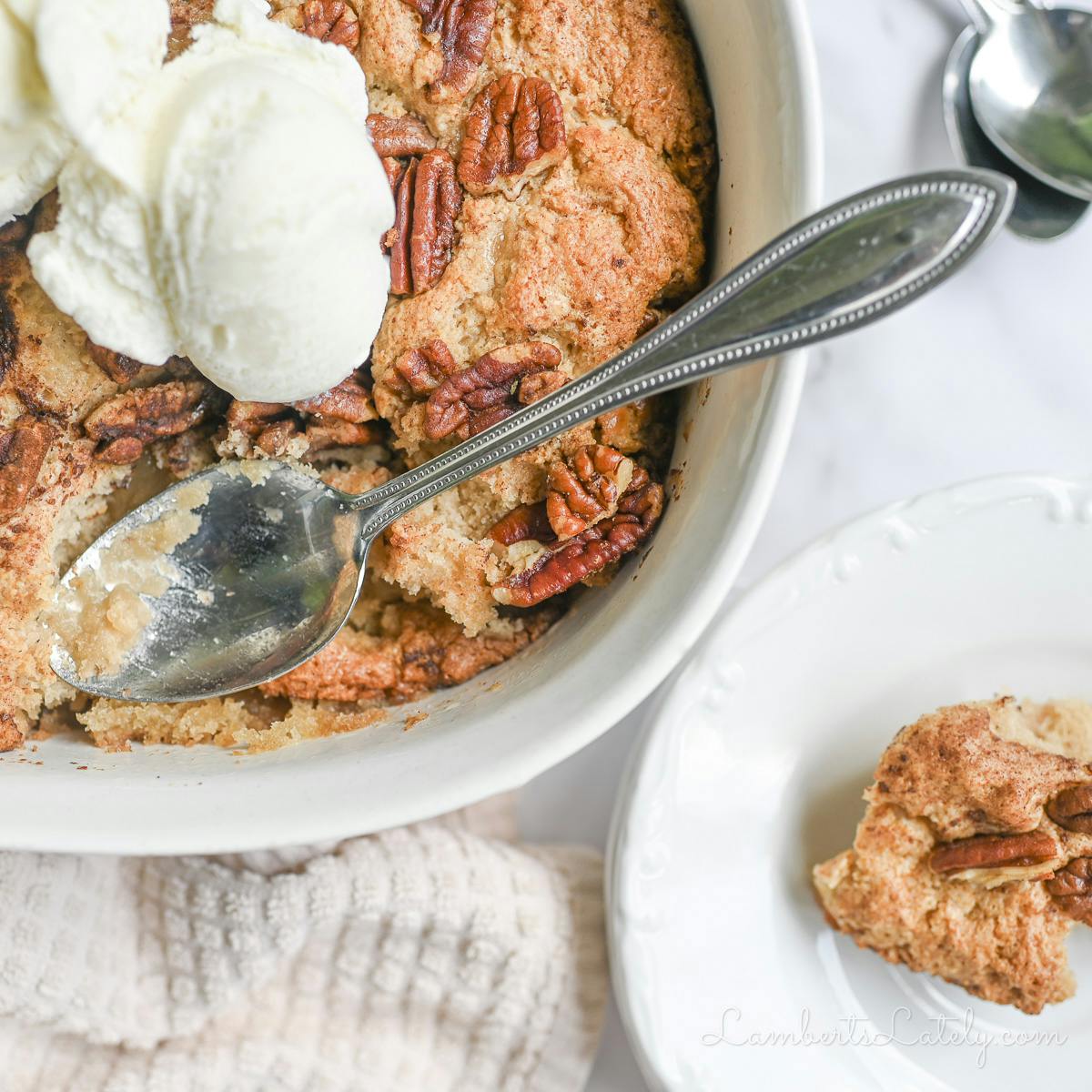 pecan cobbler in a casserole dish, with a spoon, next to plate.s