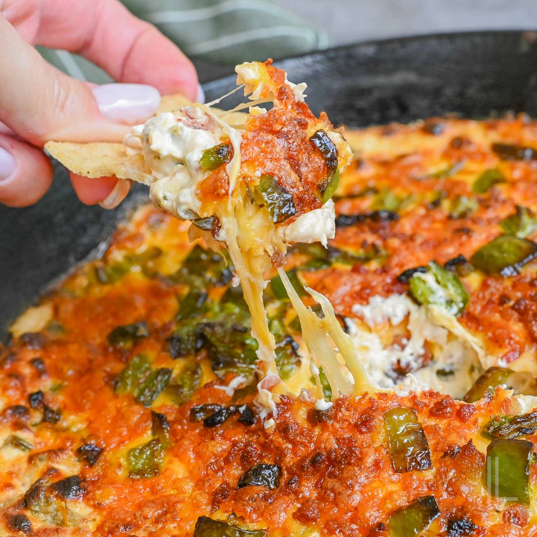 Cheesy jalapeño popper dip with roasted jalapeños, bacon, and melted cheese scooped onto a tortilla chip.
