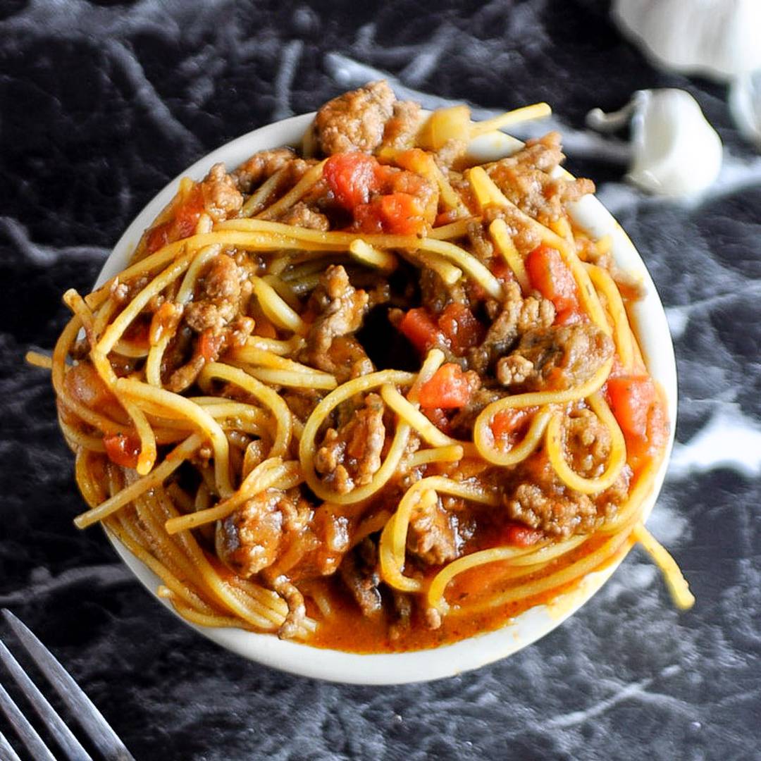 Spaghetti with ground beef and tomato sauce in a white bowl.