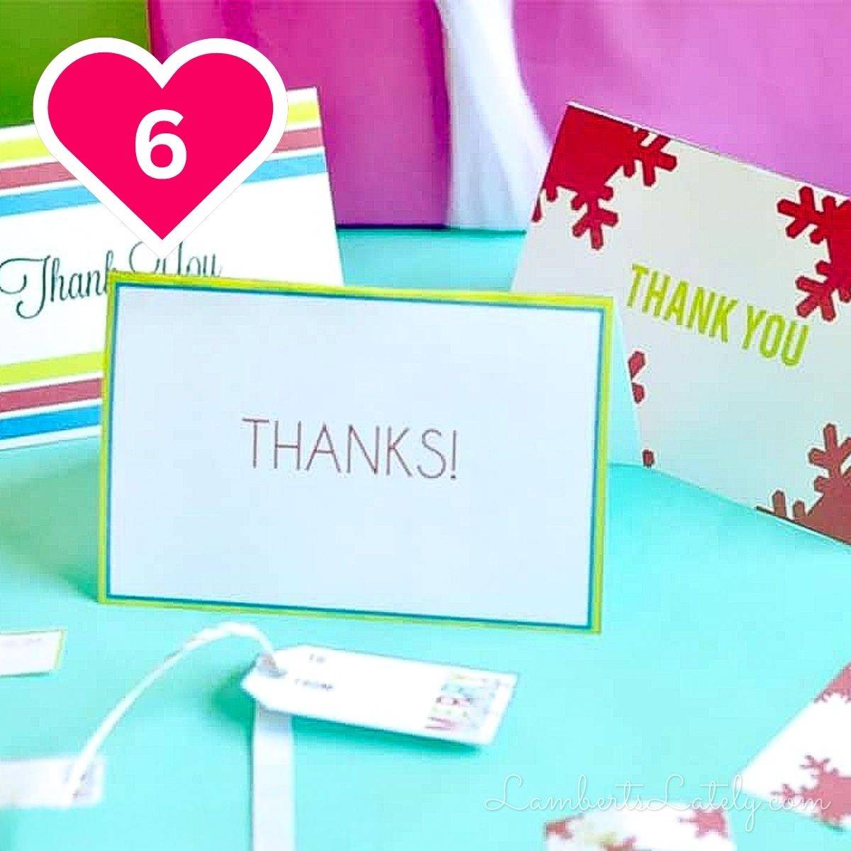 A selection of colorful handmade thank-you cards displayed on a turquoise surface. The card in the center features a simple green border and the word "THANKS!" written in a clean font. Other cards with colorful stripes and red snowflake designs are visible nearby. A pink heart icon with the number 6 is in the upper left.