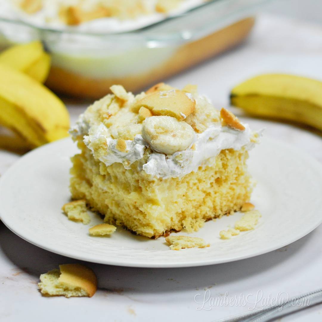 A slice of banana pudding cake topped with whipped cream, fresh banana slices, and crushed vanilla wafer cookies on a white plate, with the LambertsLately.com logo visible.