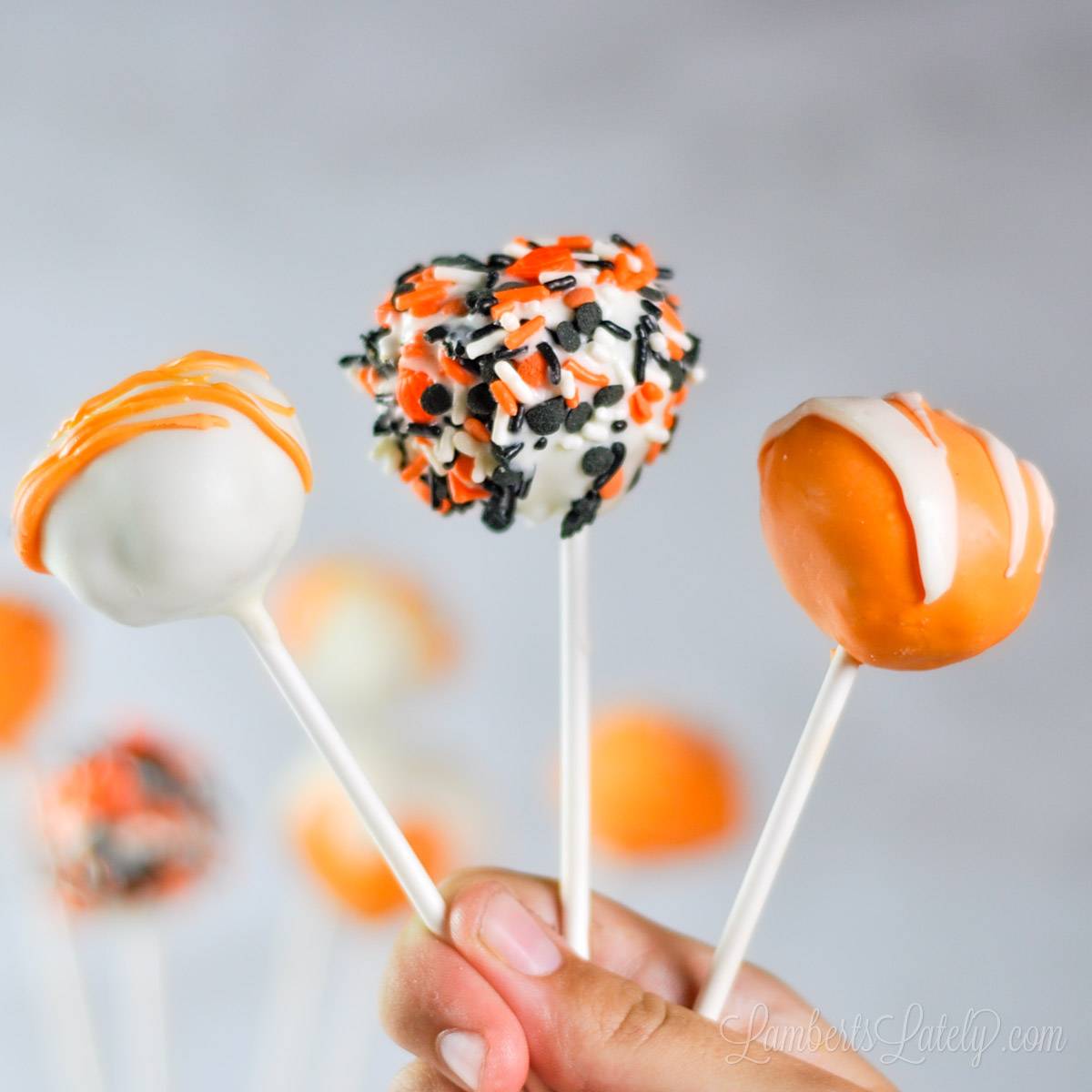 holding three pumpkin cake pops, covered in decorations.