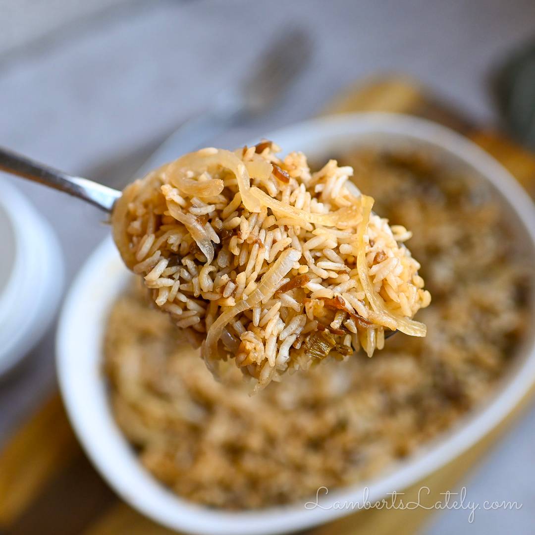 Spoonful of French onion rice over a bowl of baked rice with caramelized onions.