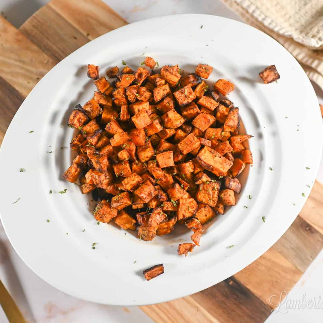Roasted sweet potato cubes seasoned with herbs and spices on a white plate.