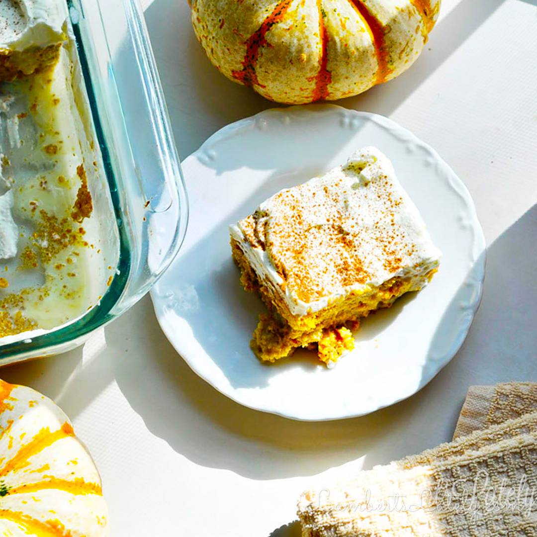 Slice of pumpkin tres leches cake with whipped topping on a white plate.