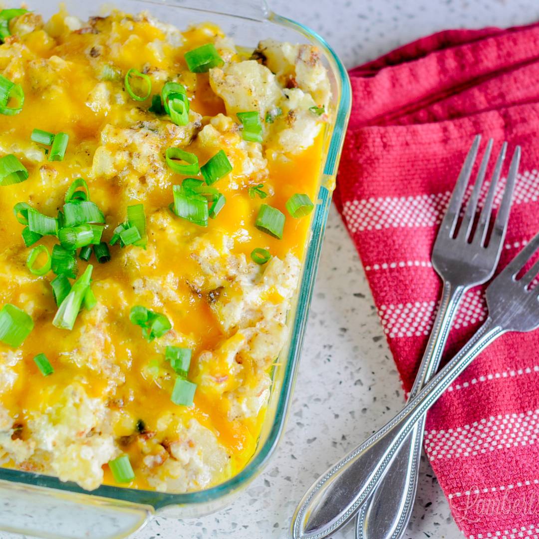 twice baked mashed potatoes in a casserole dish, next to napkin, spoons.