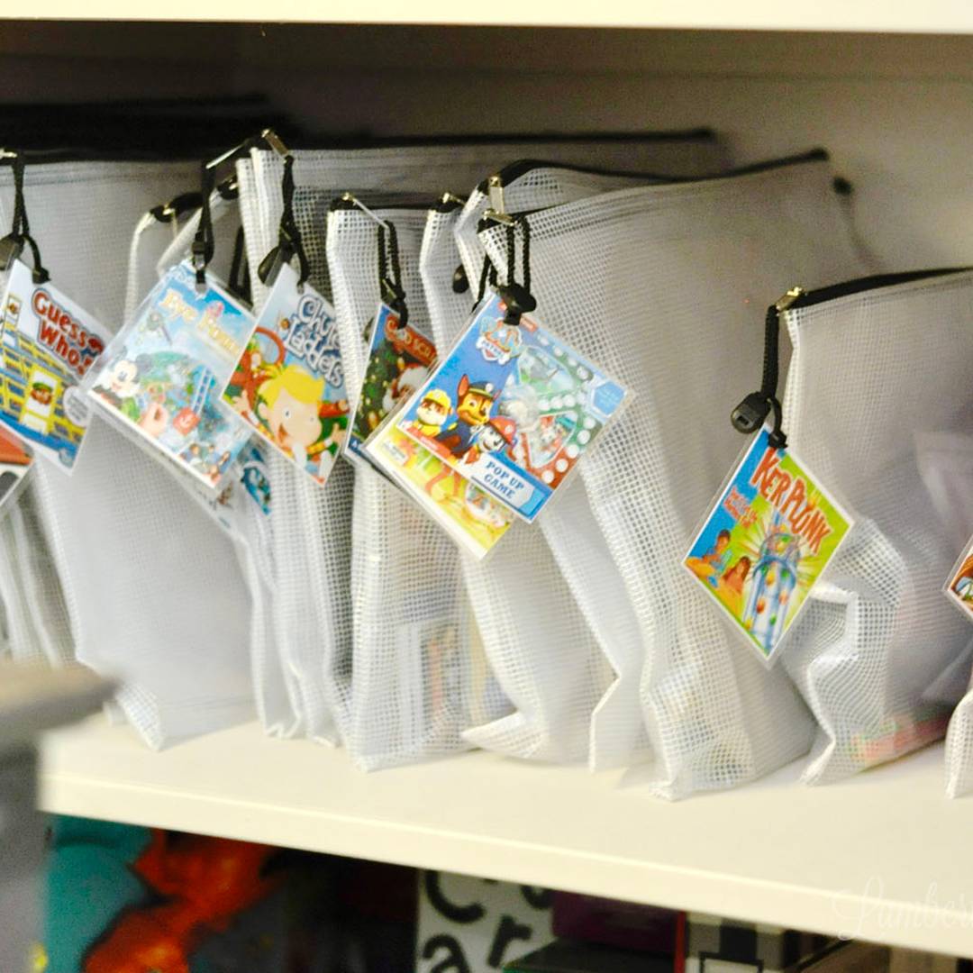 Labeled mesh storage bags hanging on a shelf, each holding a different board game for organized and space-saving game storage.