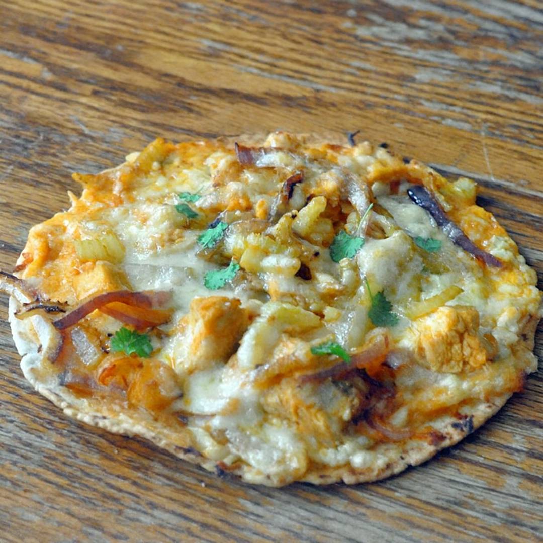buffalo chicken pizza on a tortilla, sitting on a wood surface.
